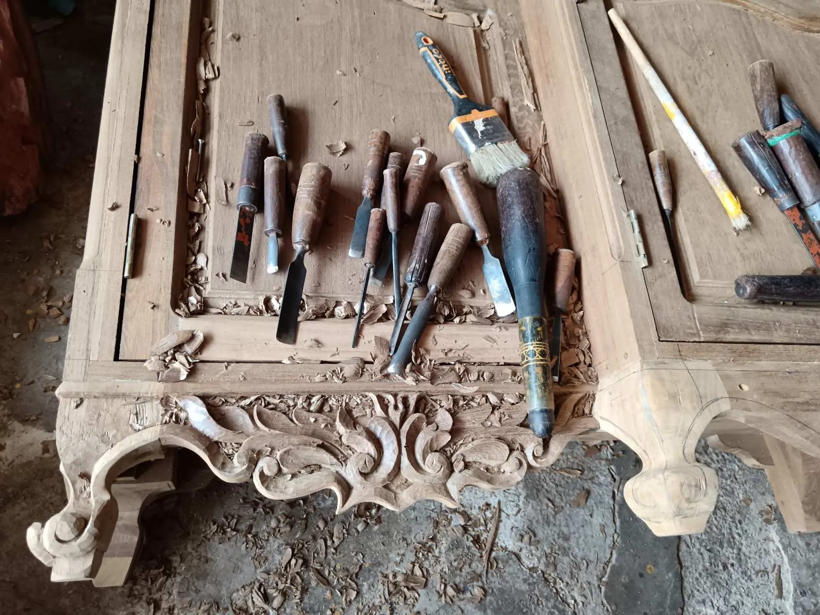 Carving chisels and brushes resting on a hand-carved wooden panel in the workshop